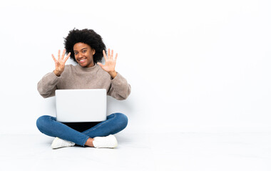 Young African American woman with a laptop sitting on the floor counting nine with fingers