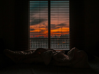 Mesmerizing view of the sunset piercing through the cloudy sky from the window blinds