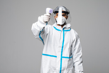Portrait of man medic wearing biological protective uniform suit clothing, mask, gloves measuring body temperature with infrared forehead thermometer gun on a white background