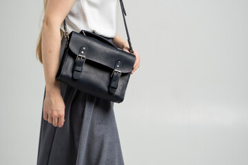 Small black leather bag over a woman shoulder on a white background. Shoulder handbag. Woman in a white shirt and grey skirt and with a black handbag. Style, retro, fashion, vintage and elegance.