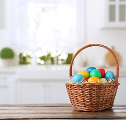 Colorful Easter eggs in wicker basket on wooden table indoors, space for text