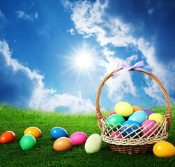 Wicker basket with Easter eggs on green grass outdoors