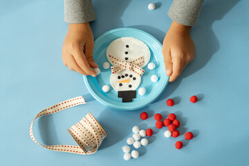 Hands of child creating a snowman with ribbon and pompom at Christmas time