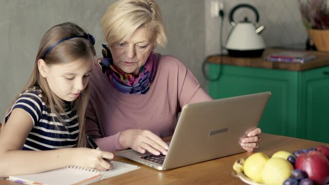 Grandmother with her young granddaughter doing homework with laptop and notebook .
