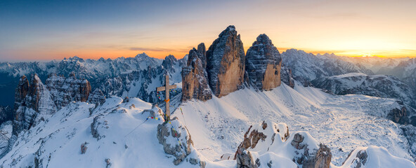 Summit cross on snow capped Monte Paterno with Tre Cime Di Lavaredo in background at sunset, Sesto Dolomites, South Tyrol