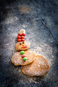 Home made pancakes in shape of snowman decorated with sugar buttons on table background at Christmas time