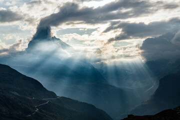 Sun rays through clouds over Matterhorn during a backlit sunset, Zermatt, Valais canton