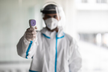 Man doctor in protective suit from the coronavirus, a medical mask glasses and gloves, uses an infrared non-contact thermometer gun to check body temperature for symptoms of the covid-19 virus 