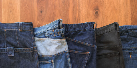 Variety of jeans and denim pants on wooden table with copyspace　様々な色や形のジーンズ・ジーパン・デニムパンツ 木製テーブル コピースペース