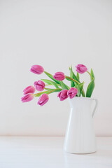 Beautiful mono bouquet of purple tulips in full bloom in white vase on white background. Copy space for text. Spring still life.