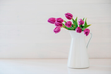 Beautiful mono bouquet of purple tulips in full bloom in white vase on white background. Copy space for text. Spring still life.