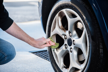 Detalle de la mano de un hombre limpiando la llanta de la rueda sucia de su coche usando una...