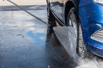 Concepto de lavado de coches. Detalle de un chorro de agua a alta presión limpiando un neumático...
