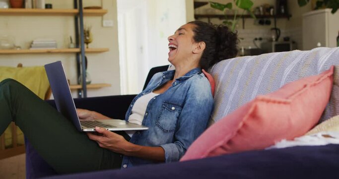 Smiling caucasian woman using laptop on video call, sitting on sofa at home