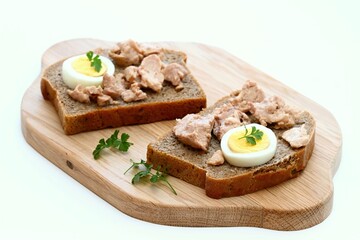 Cod liver and egg on brown bread with parsley. Healthy sandwich on cutting board. Natural source of vitamin D and omega 3, white background.