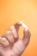Close up of man hand holding pills on orange background 