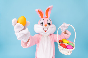 Easter bunny or rabbit or hare holds egg with basket of colored eggs, having fun, celebrates Happy...