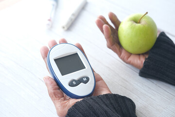  senior women holding diabetic measurement tools and apple on table 