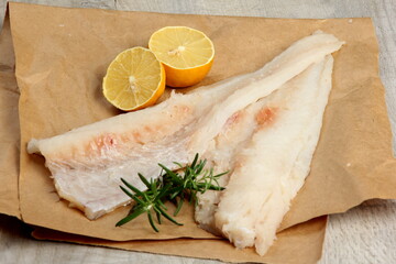 Two Piece of sea fish filet on a paper , decorated with lemon and rosemary, white raw fish filet...