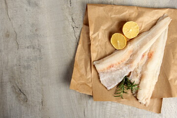 Two Piece of sea fish filet on a paper , decorated with lemon and rosemary, white raw fish filet without a skin