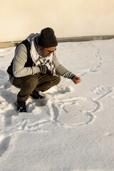 Fototapeta na wymiar Man sitting outside in the snow and painting a heart in the snow during a cold winter day
