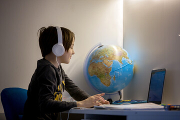 Beautiful child with earphones using laptop while studying at desk at home