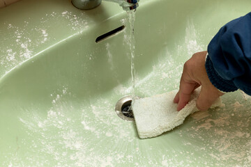 Man scrubbing a sink with a scouring pad and disinfectant powders