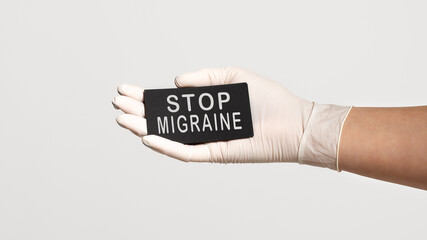 Closeup of the hand in a white sterile glove holding a card with text - STOP MIGRAINE