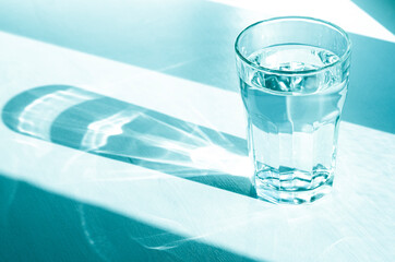 A glass with clean clear water and sharp shadows stands on a white table