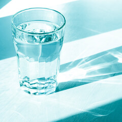 A glass with clean clear water and sharp shadows stands on a white table