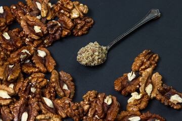 Peeled walnuts and ground walnuts on a black background. A wooden spoon full of ground walnuts. Nutritious food