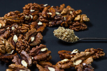 Peeled walnuts and ground walnuts on a black background. A wooden spoon full of ground walnuts. Nutritious food
