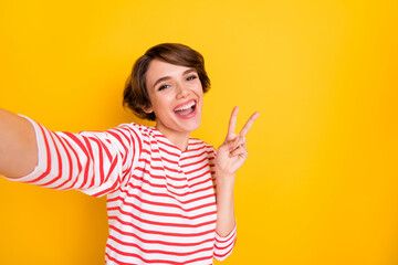 Portrait of young beautiful happy positive smiling girl take selfie showing okay sign isolated on yellow color background