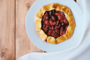 Delicious freshly baked vegan strawberry and cherry galette on wooden rustic background, top view. Sweet food, summer dessert.