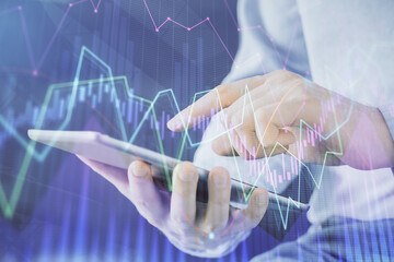 Double exposure of man's hands holding and using a digital device and forex graph drawing. Financial market concept.