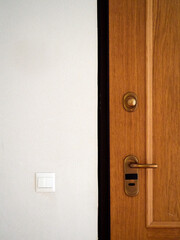Closed wooden door, gilt knob and lock. White wall with double light switch