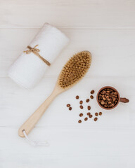 Wooden body brush, white towel and coffee beans on a white wooden background. Selective focus.