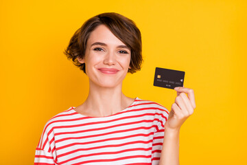 Photo of young beautiful lovely pretty cheerful smiling girl showing credit card isolated on yellow...