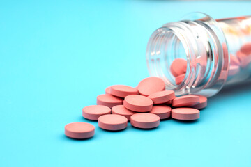 Pink pills pouring out of the medicine container on a blue background.