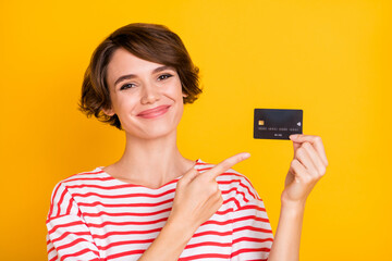 Photo of young attractive happy cheerful smiling girl recommending credit card isolated on yellow...