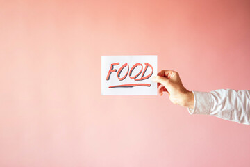 A closeup shot of a person holding a paper with the word "FOOD" on a pink background