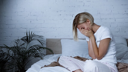 diseased woman obscuring face with hands while sneezing in bedroom