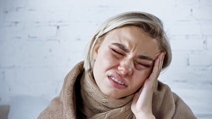 diseased woman frowning with closed eyes while suffering from headache in bedroom