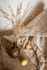 Easter still life: on a chair there is a vase with dry flowers and beige eggs next to it