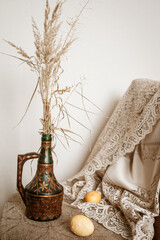 Easter still life: on a chair there is a vase with dry flowers and beige eggs next to it