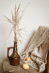 Easter still life: on a chair there is a vase with dry flowers and beige eggs next to it