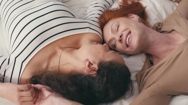 high angle view of pleased interracial lesbian couple lying on bed