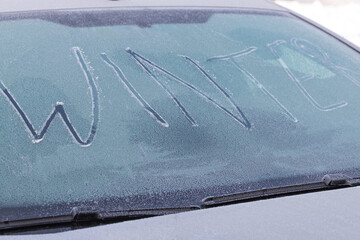the single word winter on a frozen front shield of a car