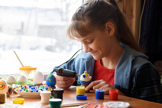 A girl glues elements to crafts with a glue gun