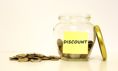 Glass jar with coins for savings. The inscription DISCOUNT on the note paper.